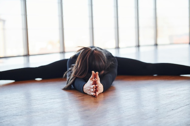 Foto donna sportiva in abiti sportivi neri sdraiata sul pavimento facendo stretching.