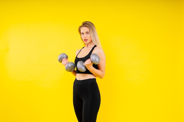 스포츠 여성 은 어두운 노란색  ⁇ 은 배경 에 있는 덤벨 으로 운동 을 한다