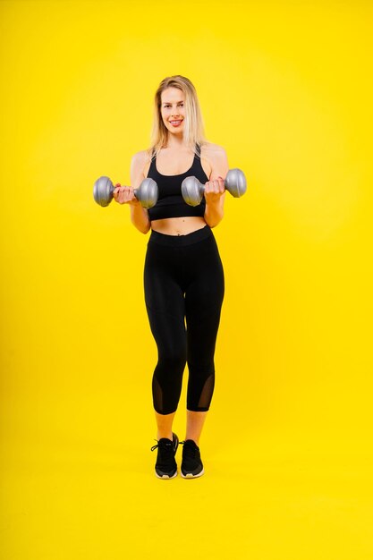 Sporty woman does the exercises with dumbbells on dark yellow red background