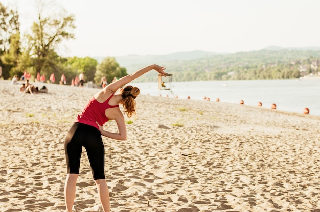 Sporty женщина делает тело растяжения на пляже, вид сзади.