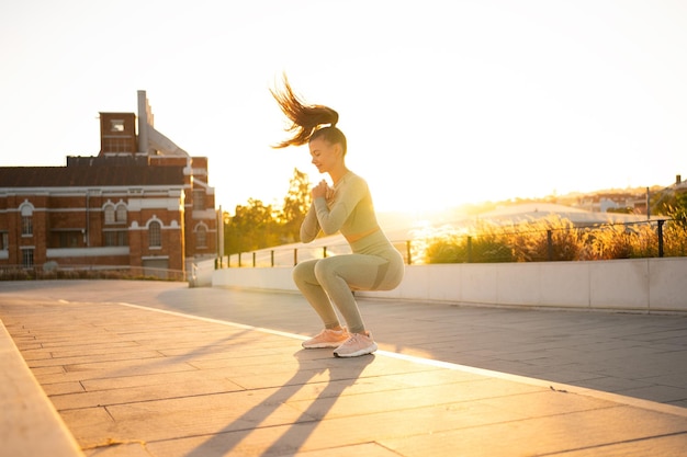 Sporty woman doing jumping squats exercises on stairs in park Bodyweight training on sunset