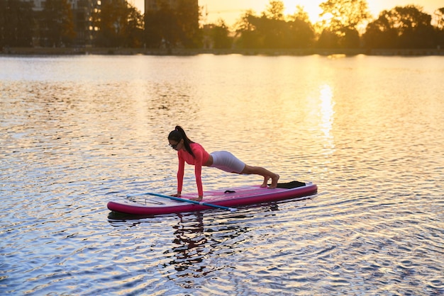 Sporty woman doing plank exercises on paddle board