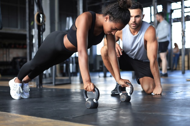 Foto donna sportiva che fa flessioni in palestra, il suo ragazzo la sta guardando.