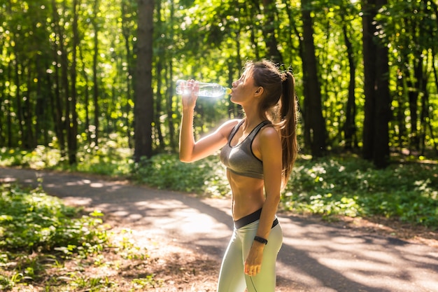 Acqua potabile della donna sportiva all'aperto il giorno pieno di sole.