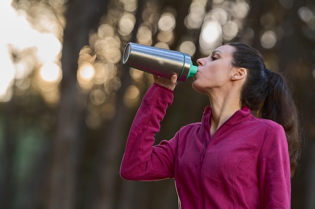 Sporty woman in the forest drinking water in recyclable ecological metal bottle eco friendly