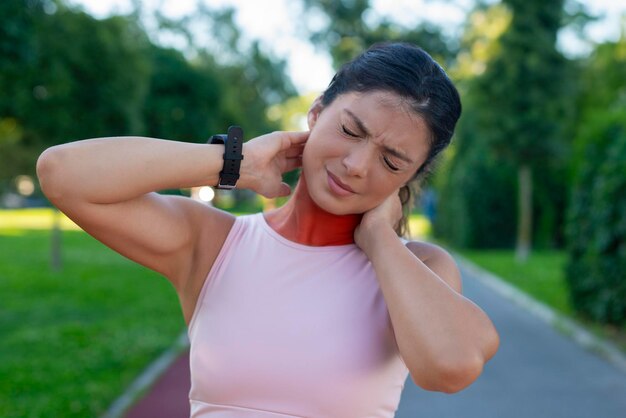 Sporty woman having the neck pain outdoors