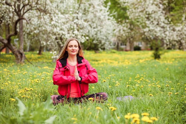 Фото Спортивная женщина занимается медитацией, сидя на зеленой лужайке среди цветущих деревьев весной.