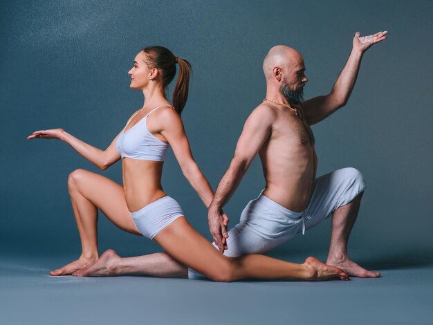 sporty woman and man in white clothes doing yoga asanas together with colorful sand indoor