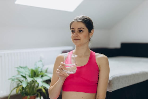 A sporty woman in a pink outfit holds a glass of water representing health and fitness