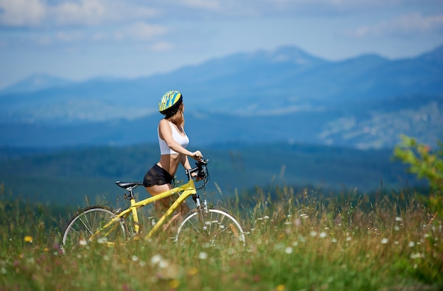 Sporty woman rider enjoying valley view with mountain bike among grass