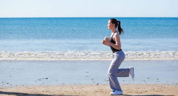 Donna sportiva che corre sulla spiaggia e ascoltare musica
