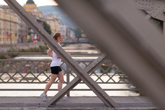 sporty woman running on sidewalk at early morning with city  sunrise scene in background