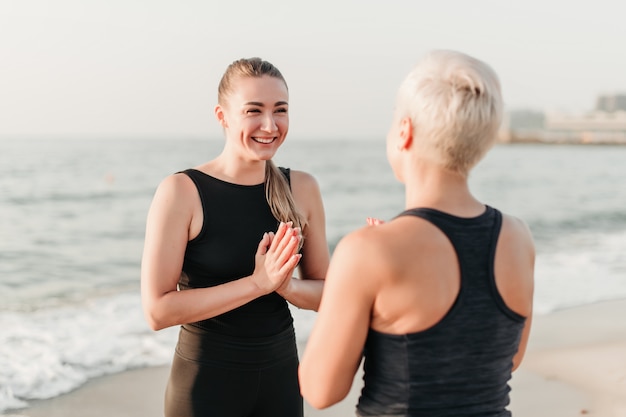 Sporty woman smiling and laughing on the beach near ocean where she meditates together with mother