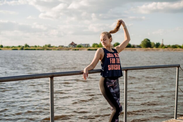 Donna sportiva in abiti sportivi che si rilassano sul molo sullo sfondo dell'acqua