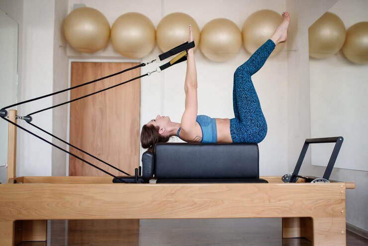 A sporty woman in sportswear is doing Pilates on a reformer in the gymSide view