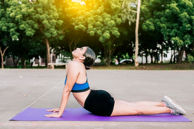 Sporty woman stretching her body doing cobra pose in a park\
athlete woman doing cobra pose in a park athlete woman doing yoga\
bhujangasana in a park