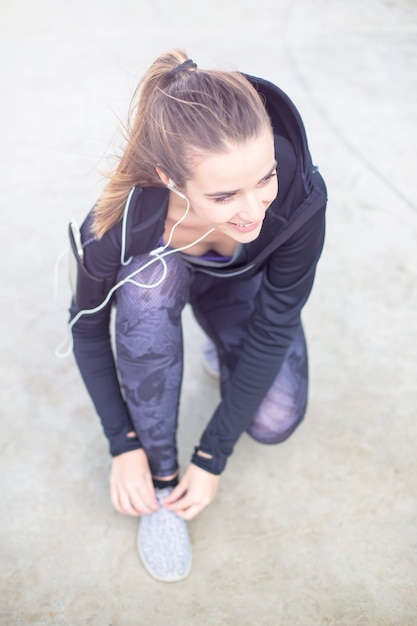 Sporty woman tying shoelace on running shoes before practice