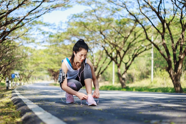 sporty woman tying shoelaces while listening to music with earphones from her smartphone 