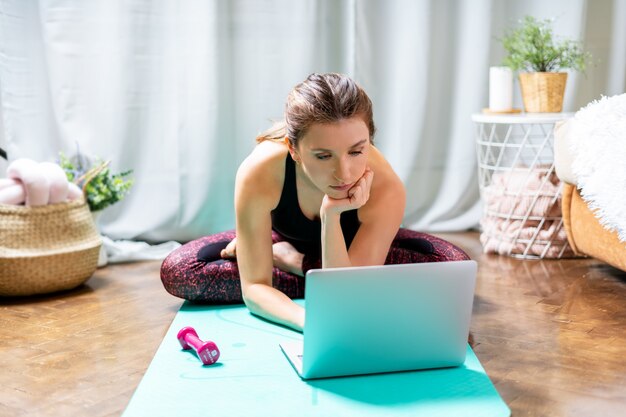 Sporty woman using her laptop while training at home.