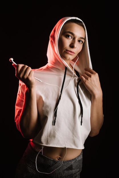 Sporty woman wearing hoodie ang earphones on black background