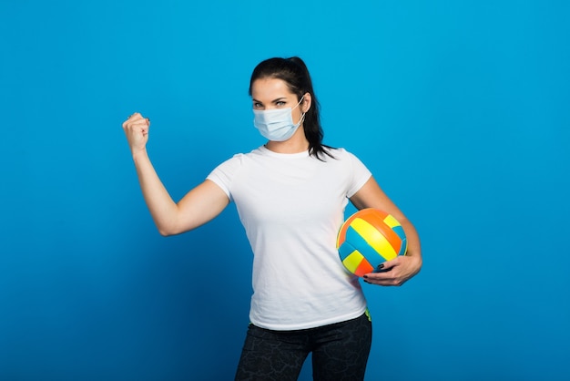 sporty woman with face mask from holding a volleyball ball