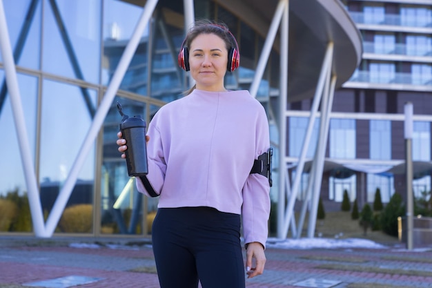 A sporty woman with headphones and a bottle of water during a\
workout outside