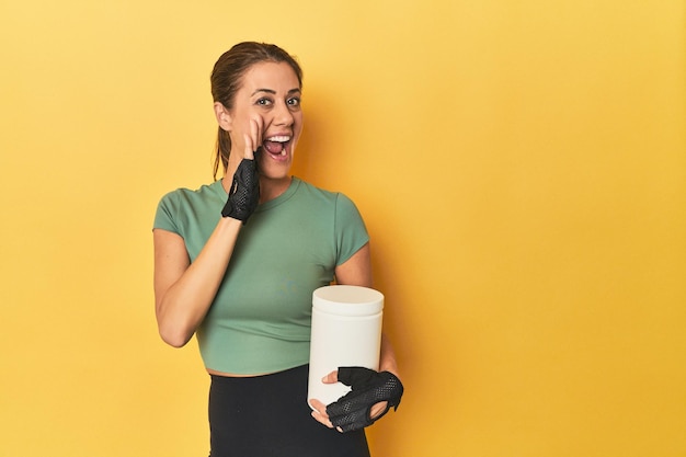 Sporty woman with protein powder jar shouting and holding palm near opened mouth