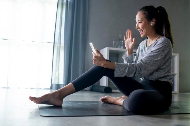 Giovane donna asiatica sportiva che si esercita a casa guardando video di fitness su internet o facendo lezione di fitness online utilizzando lo spazio della copia interna del soggiorno dello smartphone