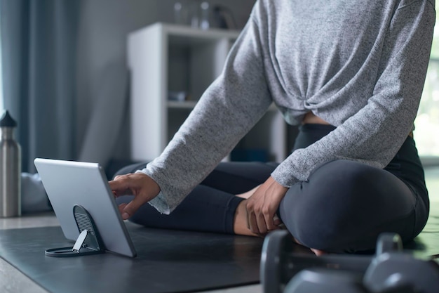 Giovane donna asiatica sportiva che si esercita a casa guardando video di fitness su internet o facendo lezione di fitness online utilizzando lo spazio interno della copia del soggiorno del tablet