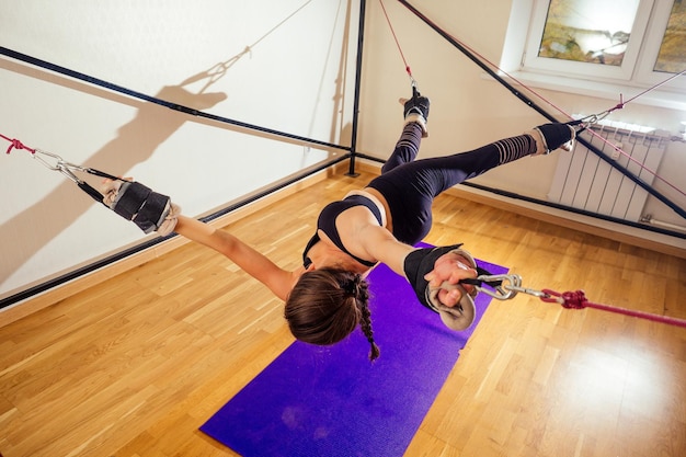 Sporty young caucasian woman doing stretching exercises of full body muscles workout on stretch aerobic aero strap in gymyogi mat