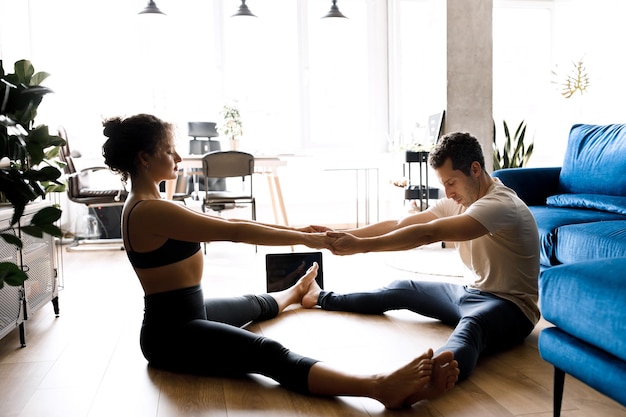 Sporty young couple warming up stretching watching fitness\
video tutorial online on laptop