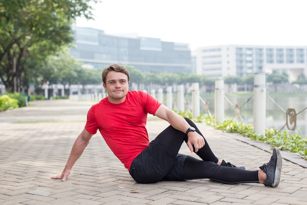 Sporty Young Man Stretching Body on Pavement