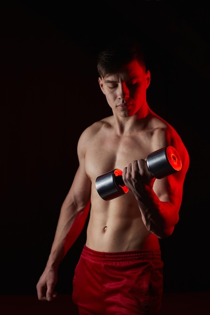 Sporty young man training with dumbbells against dark background