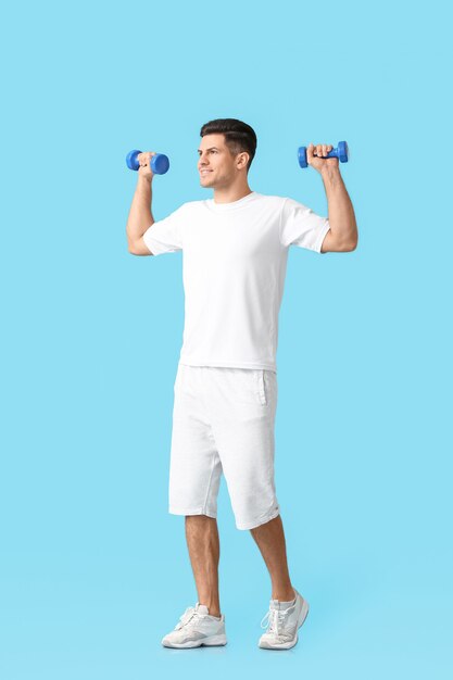 Sporty young man training with dumbbells on color surface