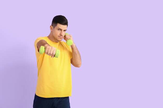 Sporty young man training with dumbbells on color surface