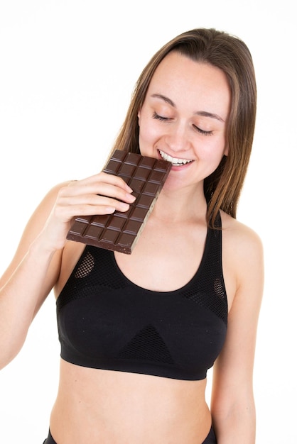 Sporty young woman biting chocolate isolated on white background