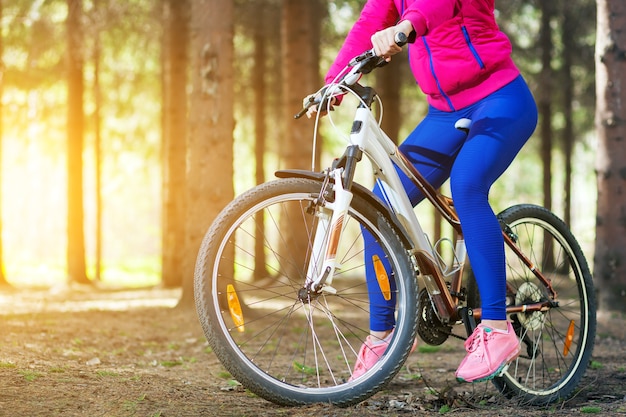 Sporty young woman in a bright pink jacket and jeans rides a bike through the forest