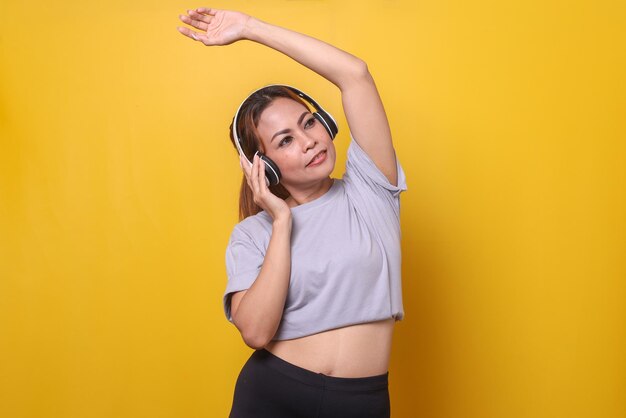 Sporty young woman dancing with headphones on yellow background