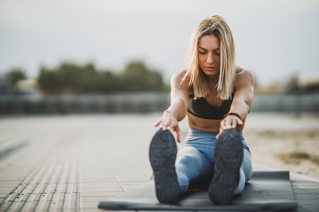 Sporty young woman doing stretching exercises while warming up before training outdoor.