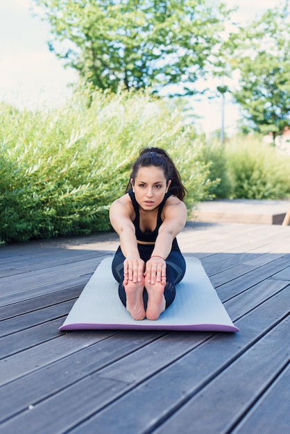 La giovane donna sportiva fa l'esercizio di yoga con la stuoia di yoga al concetto di stile di vita attivo all'aperto del parco