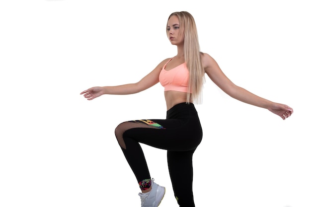 A sporty young woman in a pink top leggings and sneakers does exercises on a white background