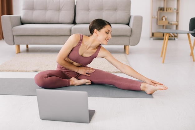 Sporty young woman practicing yoga in front of laptop watching\
online tutorials