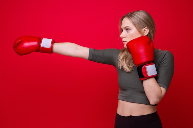 Sporty young woman in red boxing gloves practicing punches