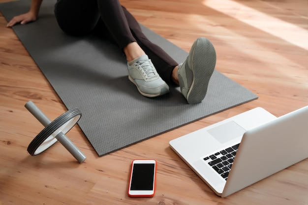 Фото Спортивная молодая женщина сидит на коврике для упражнений и смотрит онлайн-тренировки