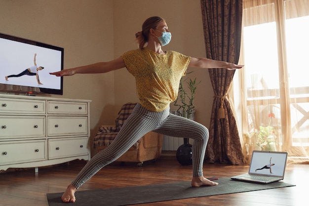 Giovane donna sportiva che prende lezioni di yoga online e si esercita a casa durante la quarantena. concetto di stile di vita sano, benessere, sicurezza durante la pandemia di coronavirus, ricerca di nuovi hobby.