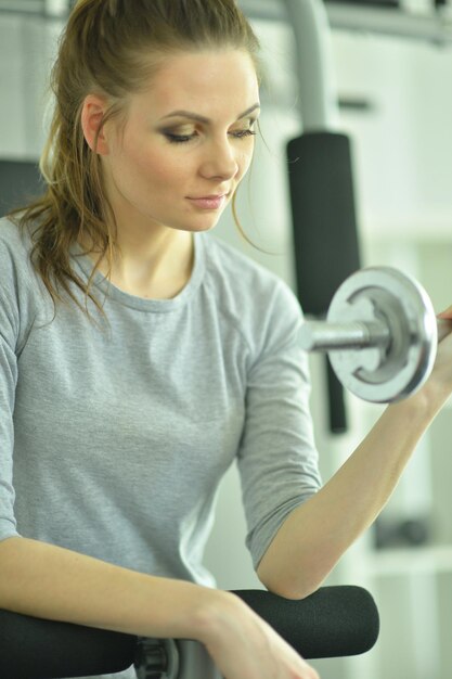 Sporty young woman training with dumbbell in gym