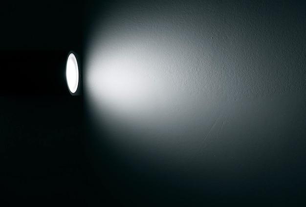 Photo spotlight lamp with beam of light on the wall in dark room