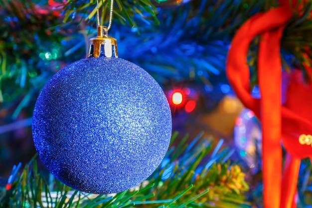 Sprankelende blauwe kerstbal en rood lint op takken van decoratieve sparclose-up