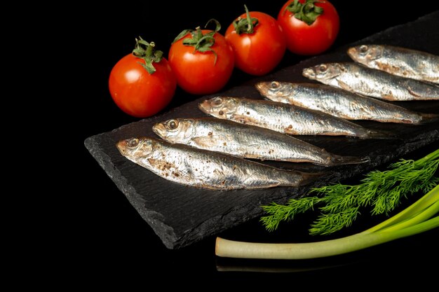 Sprat with vegetables on a serving black board Small salted fish with vegetables