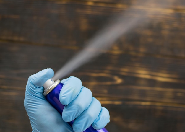 Spray the aerosol from the can with a hand in a rubber glove against a dark background